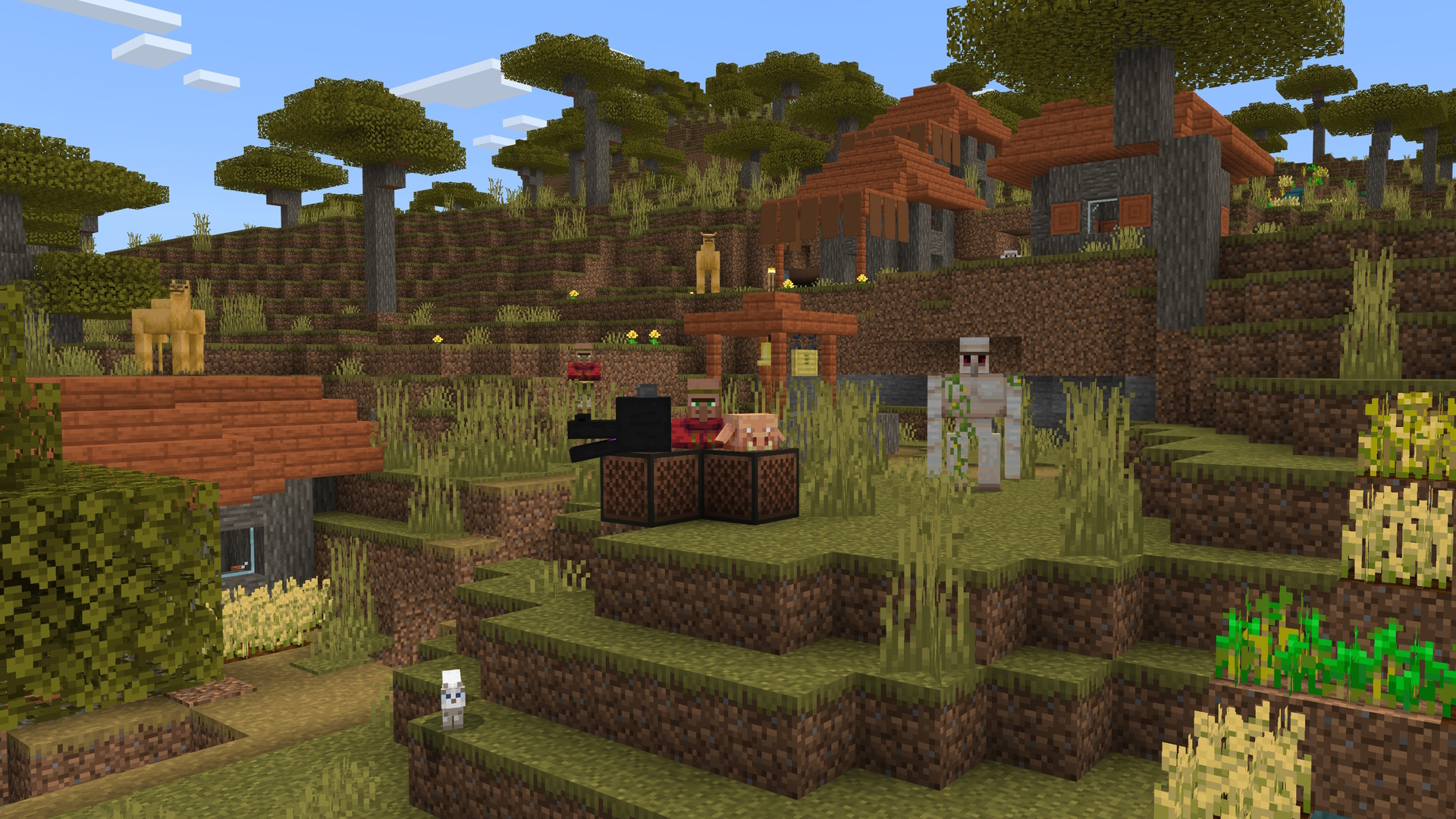 A Minecraft screenshot of a village, featuring a villager standing by two noteblocks with a dragon and a piglin head on top. There is an iron golem, two camels, and a cat in the scene also.
